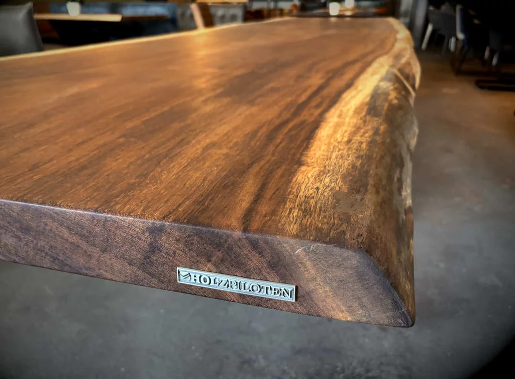 Holzpiloten-Schild auf der Stirnseite der Kambala Tischplatte mit natürlicher Baumkante